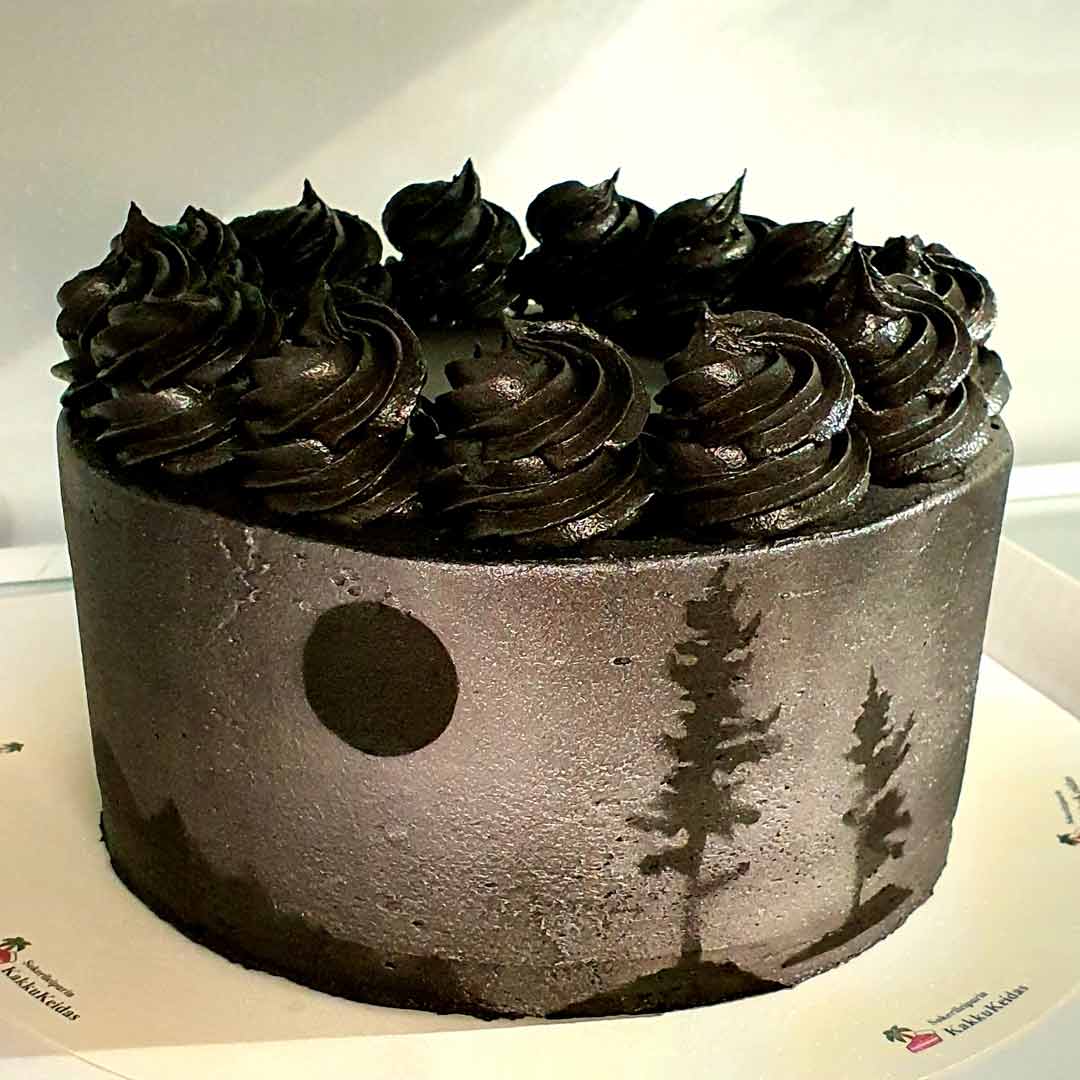 Musta-hopea kakku, jonka kyljessä on puiden siluetteja ja päällä kermavaahtokierteitä