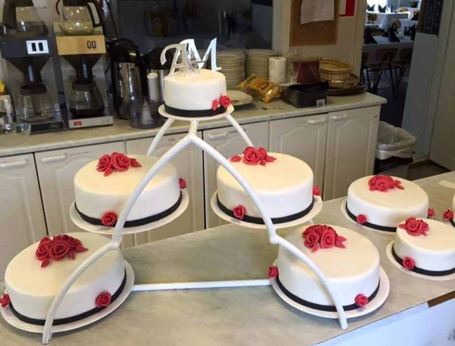 Monikerroksiseen kakkutelineeseen laitettuja valkeita kakkuja, jotka on koristeltu massasta tehdyillä ruusuilla
