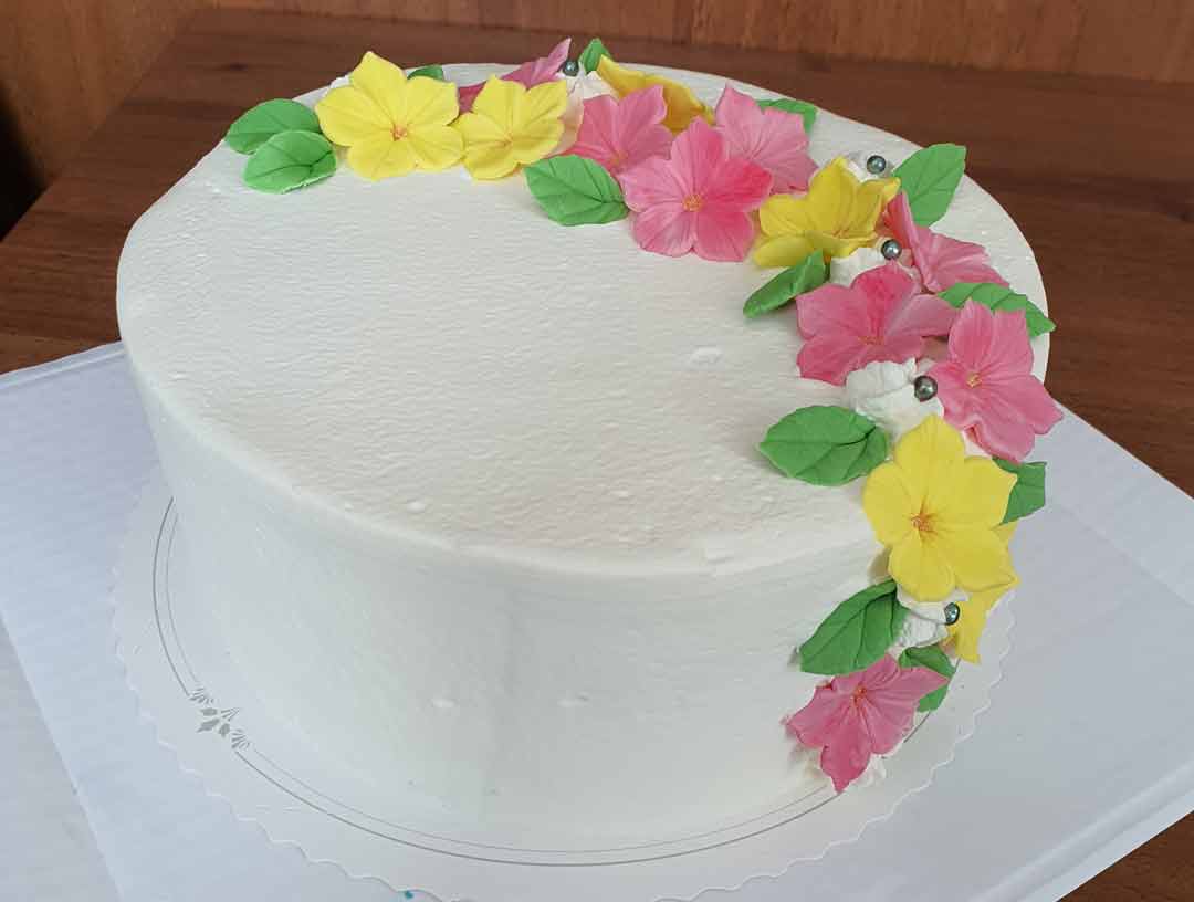 Valkea kakku, joka on koristeltu värikkäästä massasta tehdyillä kukilla