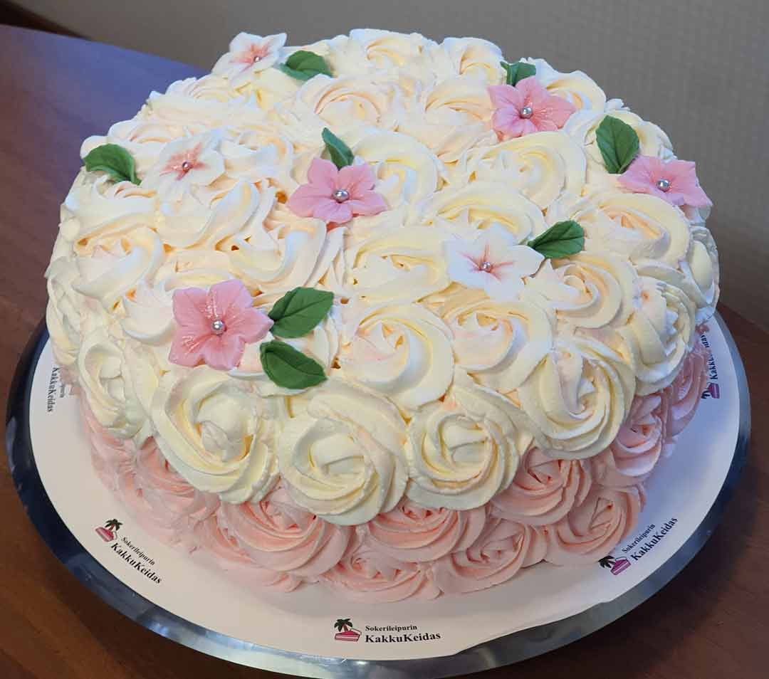 Valkoisilla ja vaaleanpunaisilla kermakierteillä sekä massasta tehdyillä kukilla koristeltu kakku