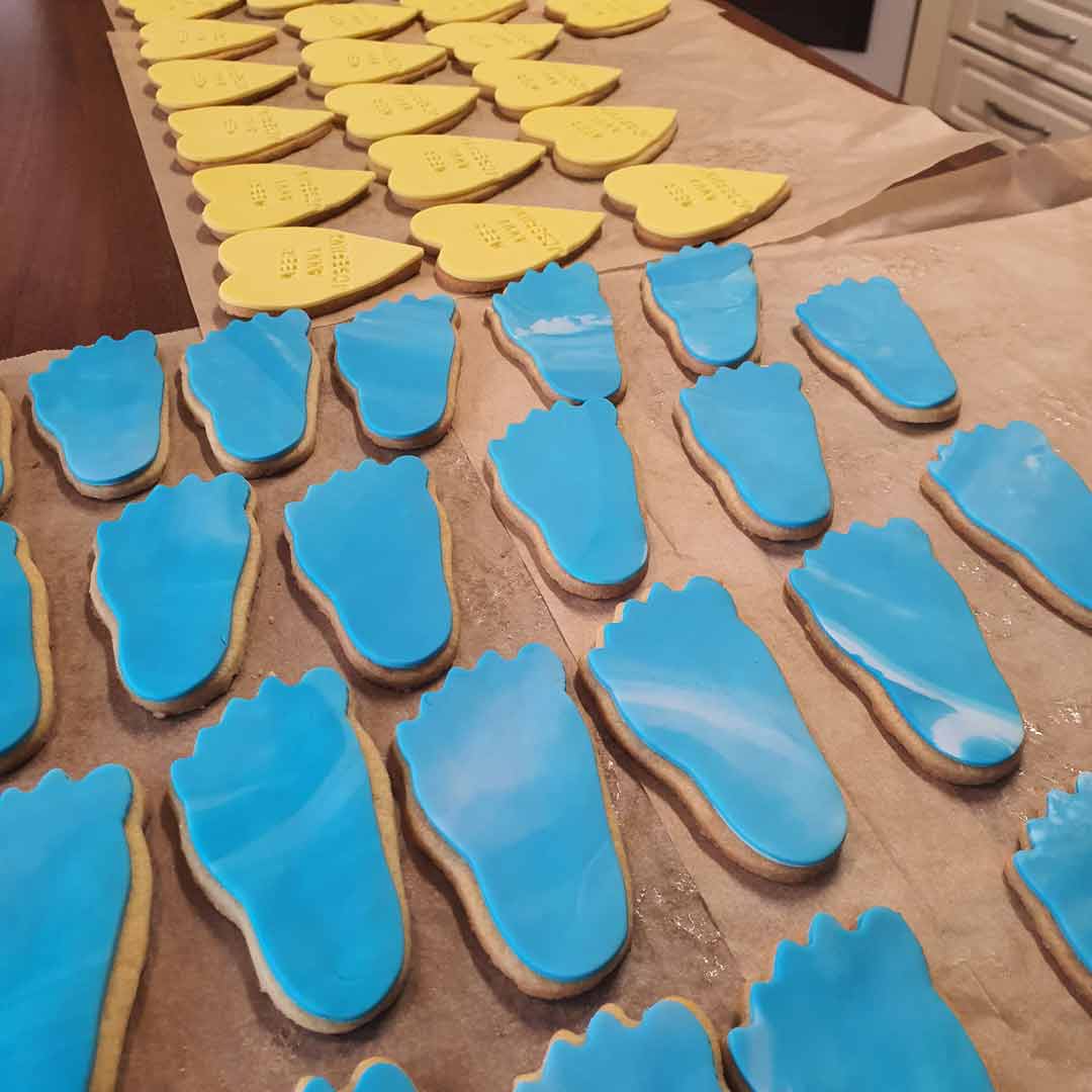 Sinisiä jalan muotoisia keksejä ja keltaisia nimikeksejä